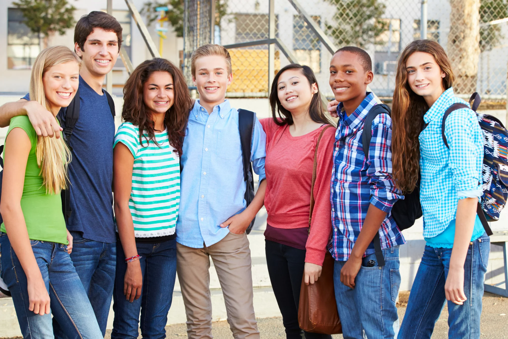 Group Of Teenage Pupils Outside Classroom With Arms Round Each Other Smiling At Camera